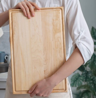 A woman holding a wooden cutting board in the kitchen.