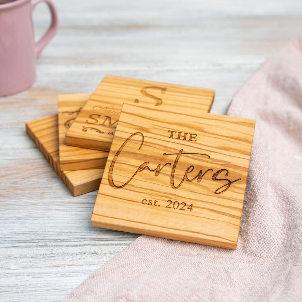 Custom wooden coasters engraved with the name "the carters est. 2024" on a table next to a pink mug.