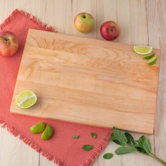 A wooden cutting board with limes and apples.