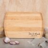 Personalized engraved wood cutting board with engraving in the lower right corner and leaning over a wall.