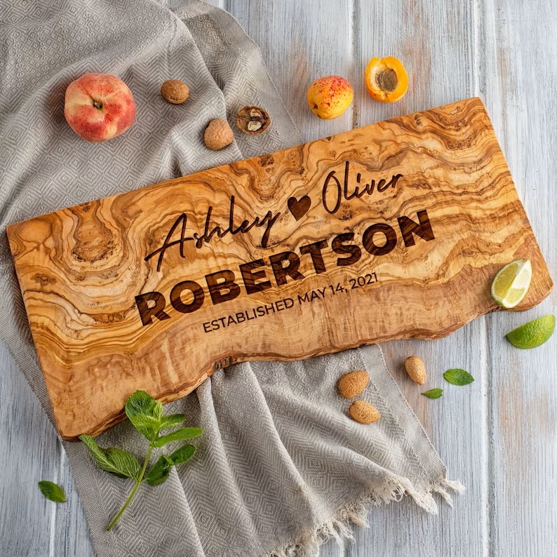 Personalized wedding gift olive wood live edge cutting board with the couple's first names and last name underneath.