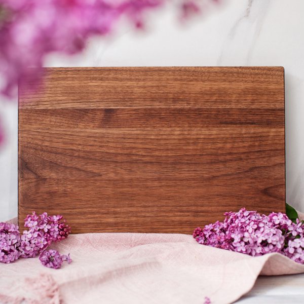 A wooden cutting board with purple lilies on it.
