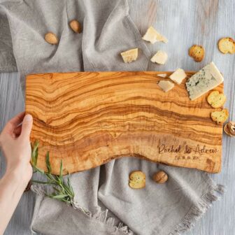 A person holding a wooden cutting board with rosemary and crackers.