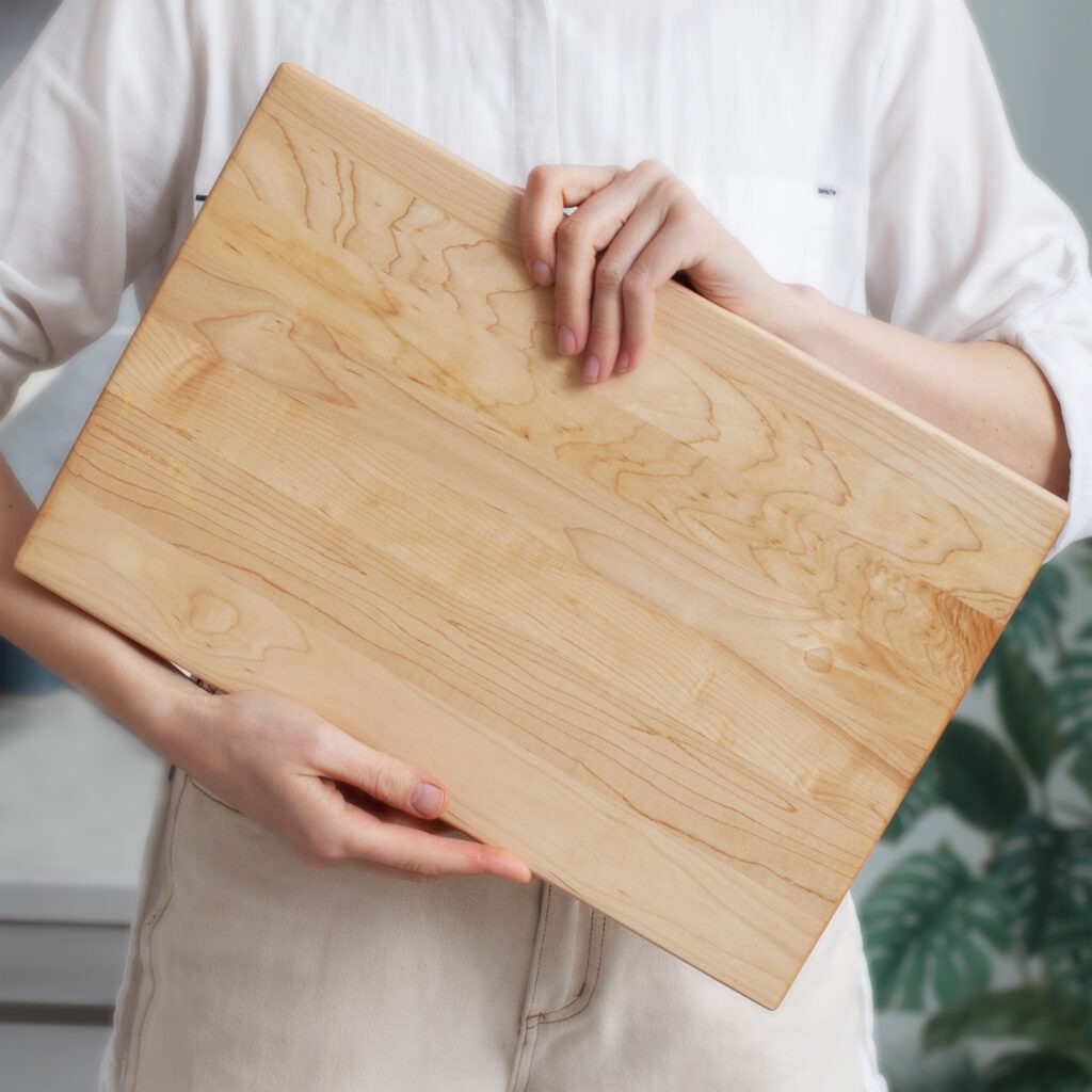 A woman holding a wooden cutting board.