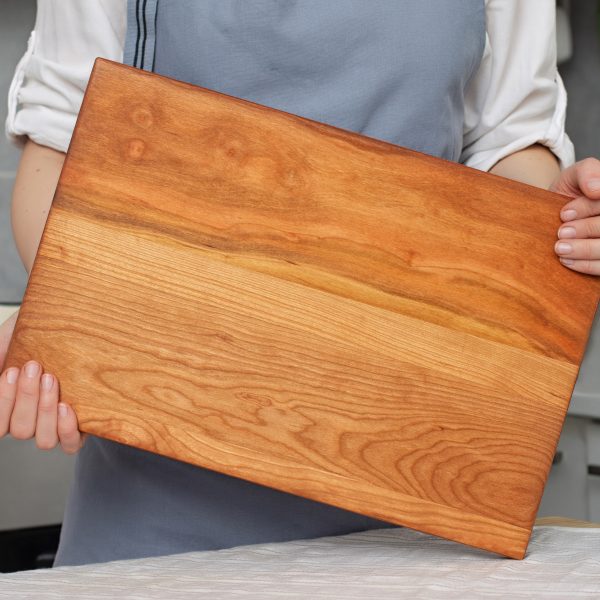 A woman is holding a wooden cutting board.