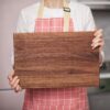 A woman is holding a wooden cutting board.
