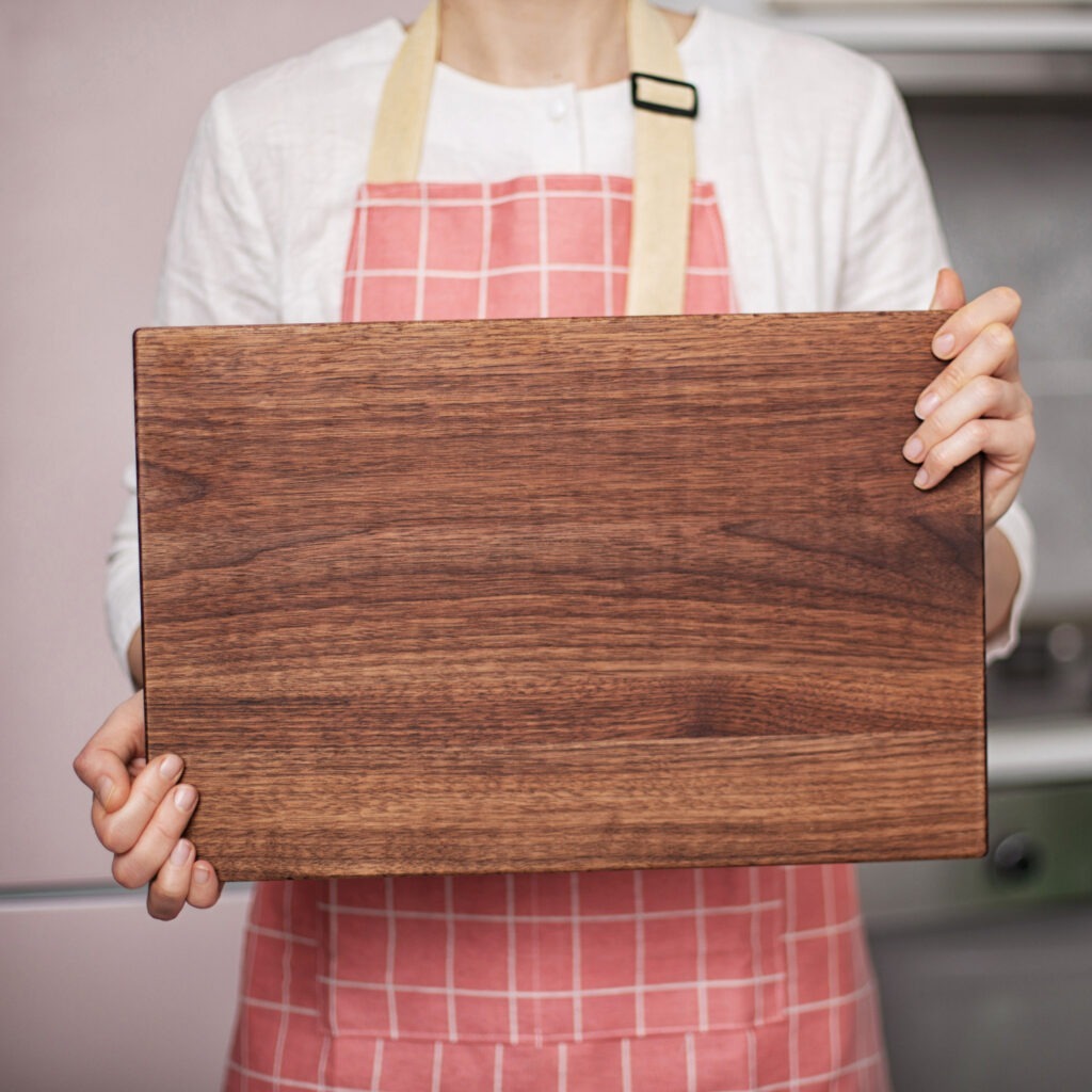 A woman is holding a wooden cutting board.