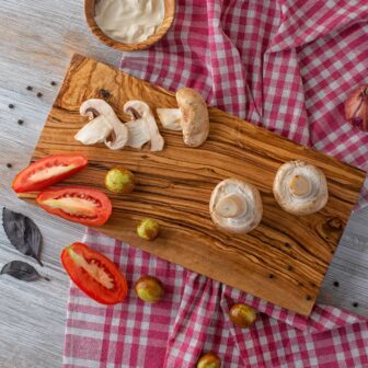 A rectangular wooden cutting board with mushrooms and tomatoes on it.