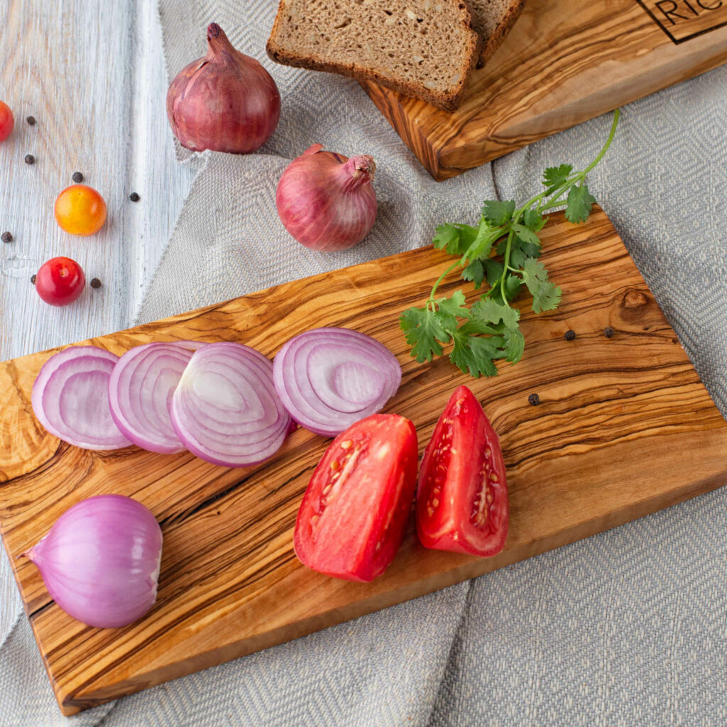 A Rectangular Olive Wood Cutting Board with tomatoes, onions and bread.