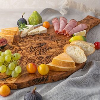An Olive Wood Charcuterie Board with fruit, ham and cheese.