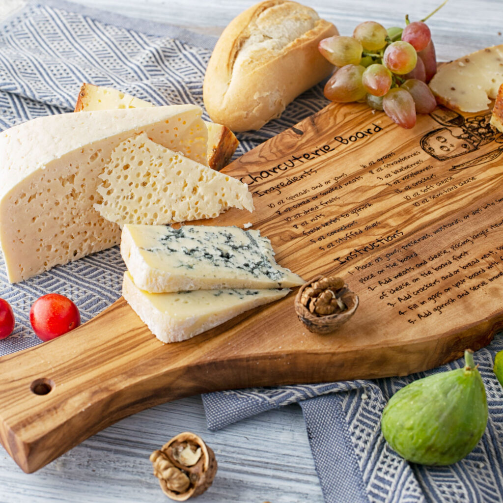 A wooden Engraved Serving Charcuterie Board with a variety of cheeses on it.