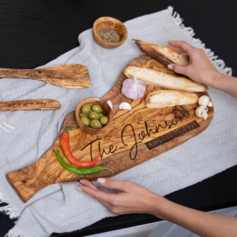 A person is holding a Personalized Olive Wood Charcuterie Board with a fish on it.