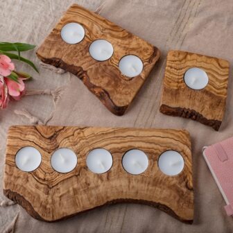 Three wooden candle holders on a bed with flowers and a notebook.