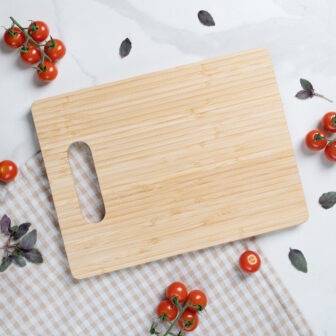 A wooden cutting board on a marble surface surrounded by cherry tomatoes and basil leaves.