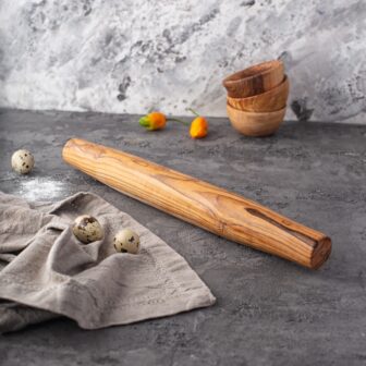 A wooden rolling pin on a table next to eggs.