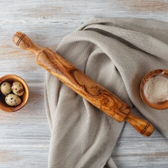 An olive wood rolling pin and eggs on a wooden table.