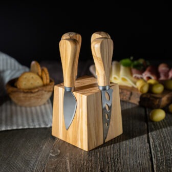 Three cheese knives on a wooden block on a wooden table.