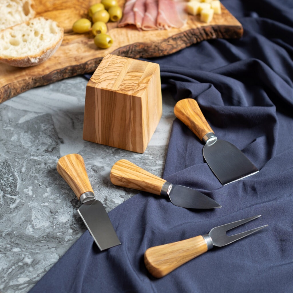 A set of cheese knives and a block of cheese on a table.