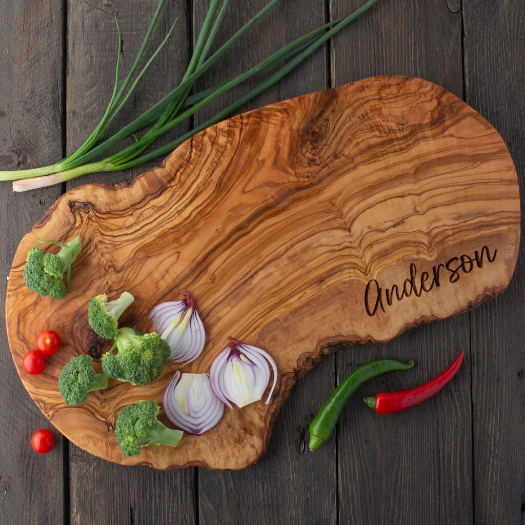 A personalized olive wood cutting board with vegetables on it.