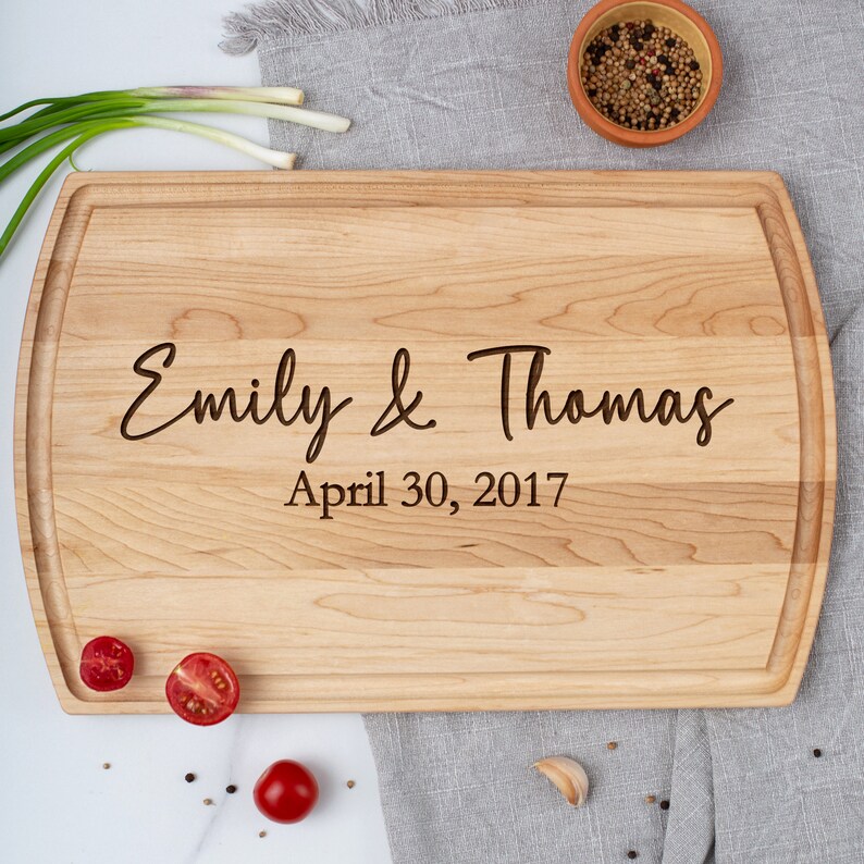 Arch-shaped maple cutting board with engraved couple's first names and the date underneath.