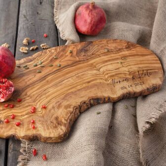 A wooden cutting board with pomegranates and pomegranate seeds.