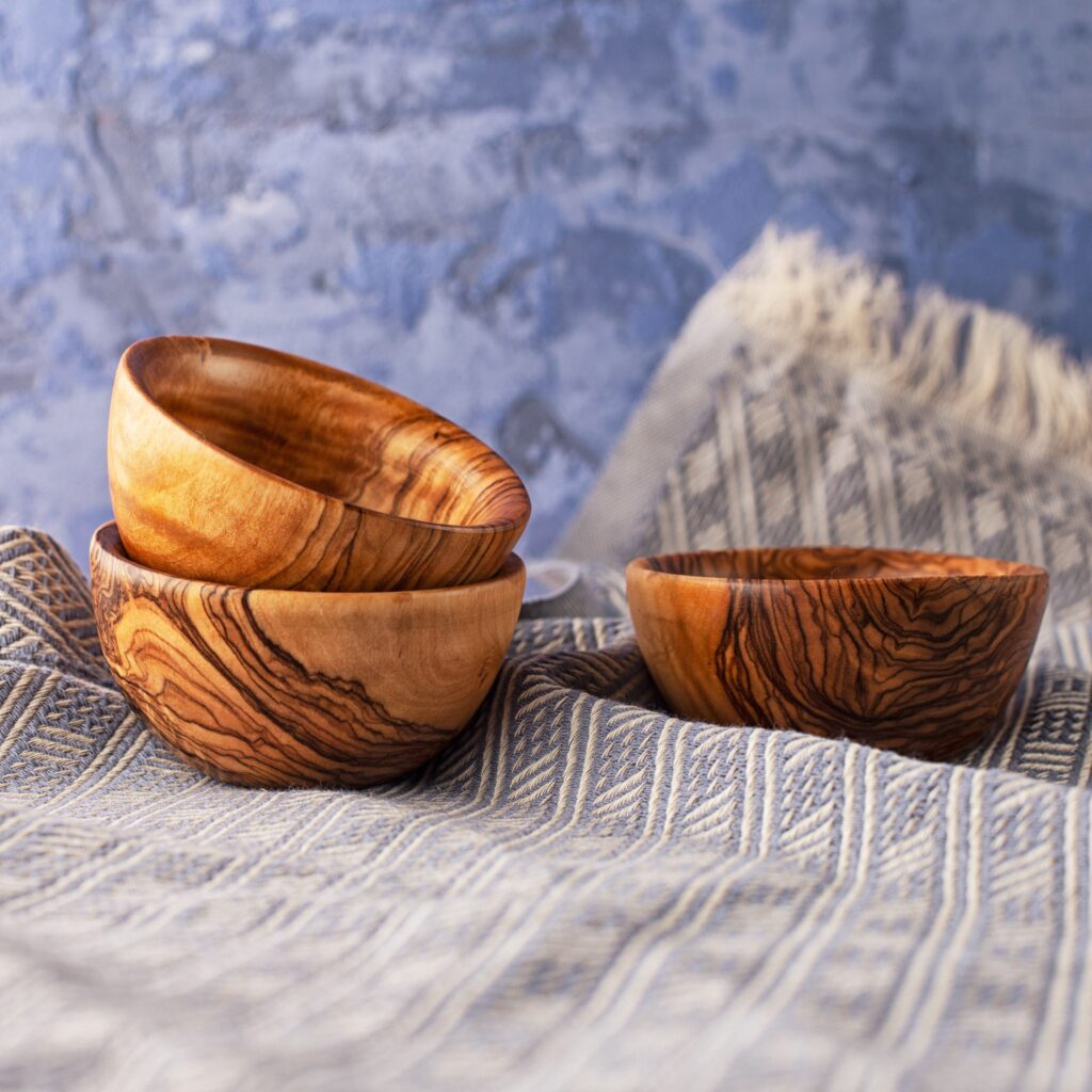 Three olive wood bowls on a blue cloth.