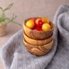 A wooden bowl filled with cherries on a blue cloth.