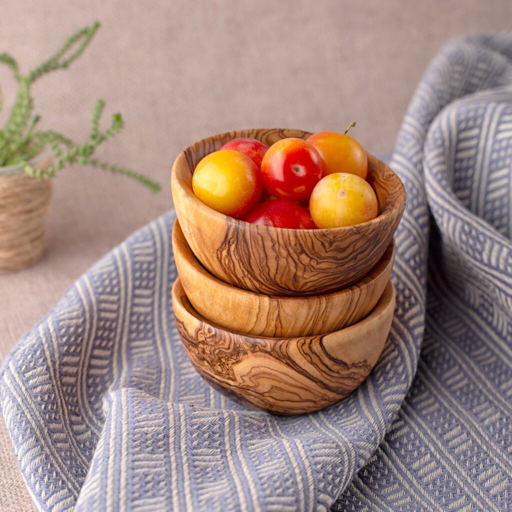 A wooden bowl filled with cherries on a blue cloth.
