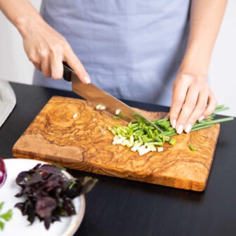 A woman cutting vegetables on a Rectangular Olive Wood Cutting Board.