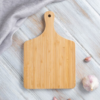 Wooden cutting board on a light wooden surface with a garlic bulb nearby.
