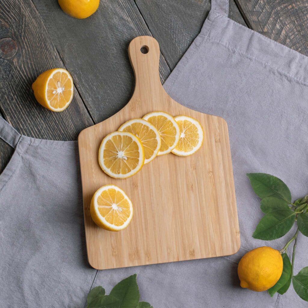 Sliced lemons neatly arranged on a wooden cutting board with a grey apron and additional lemons in the background.