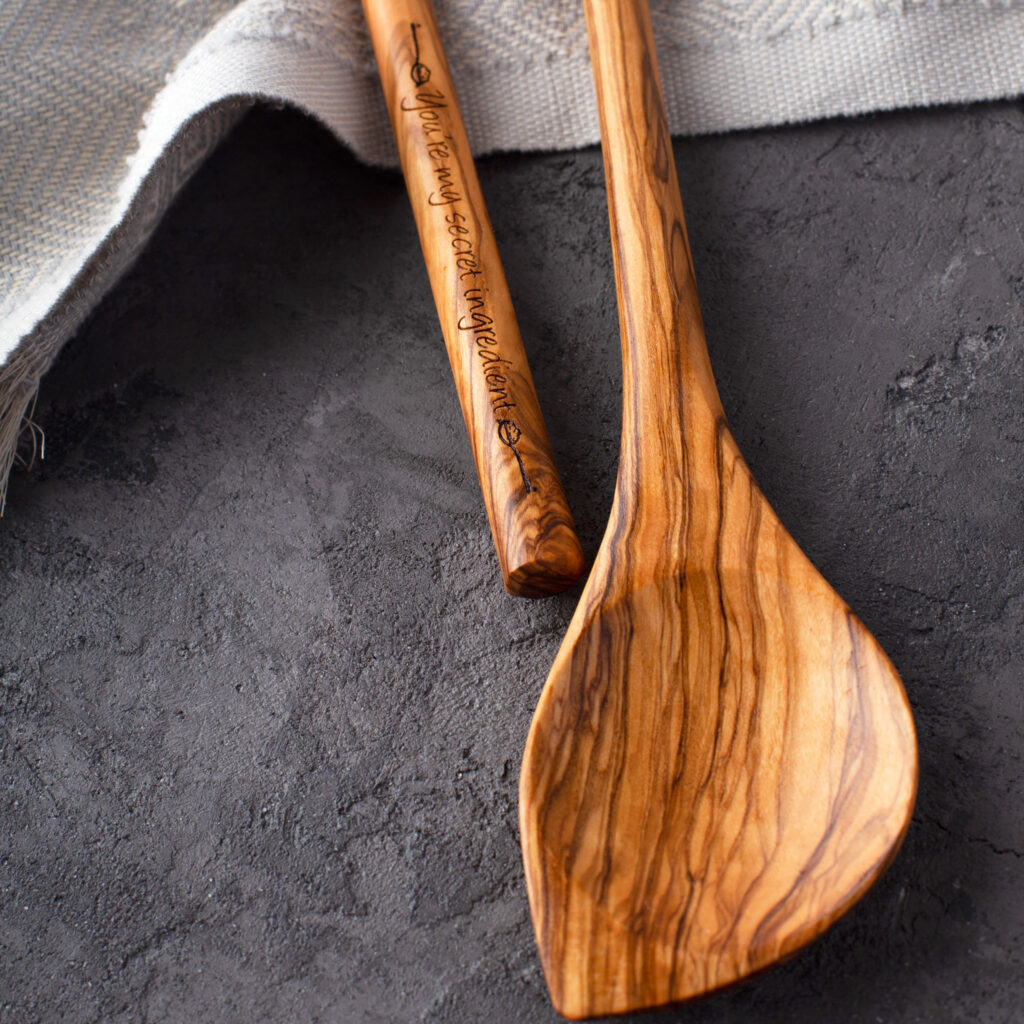Engraved Olive Wood Spoons (Corner) – Set of 2 on a table next to a cloth.
