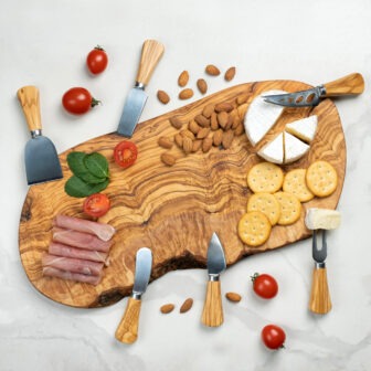 A wooden board with cheese, crackers, tomatoes and olives.