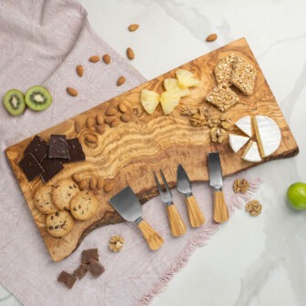 A wooden cheese board with fruit and nuts on it.
