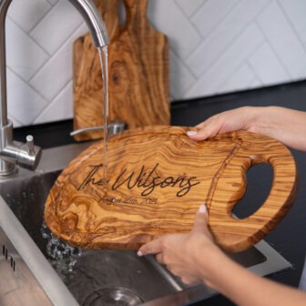 A woman is washing a wooden cutting board in a kitchen sink.