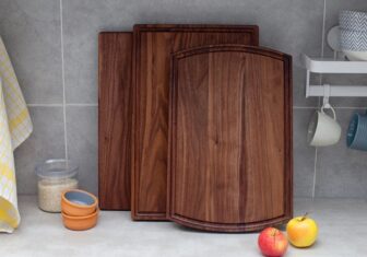 Three walnut cutting boards of various styles leaning over the backsplash on the kitchen counter.