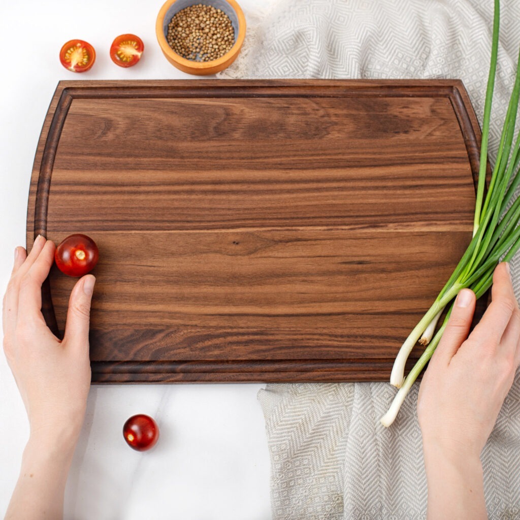 A person holding a wooden cutting board with onions on it.