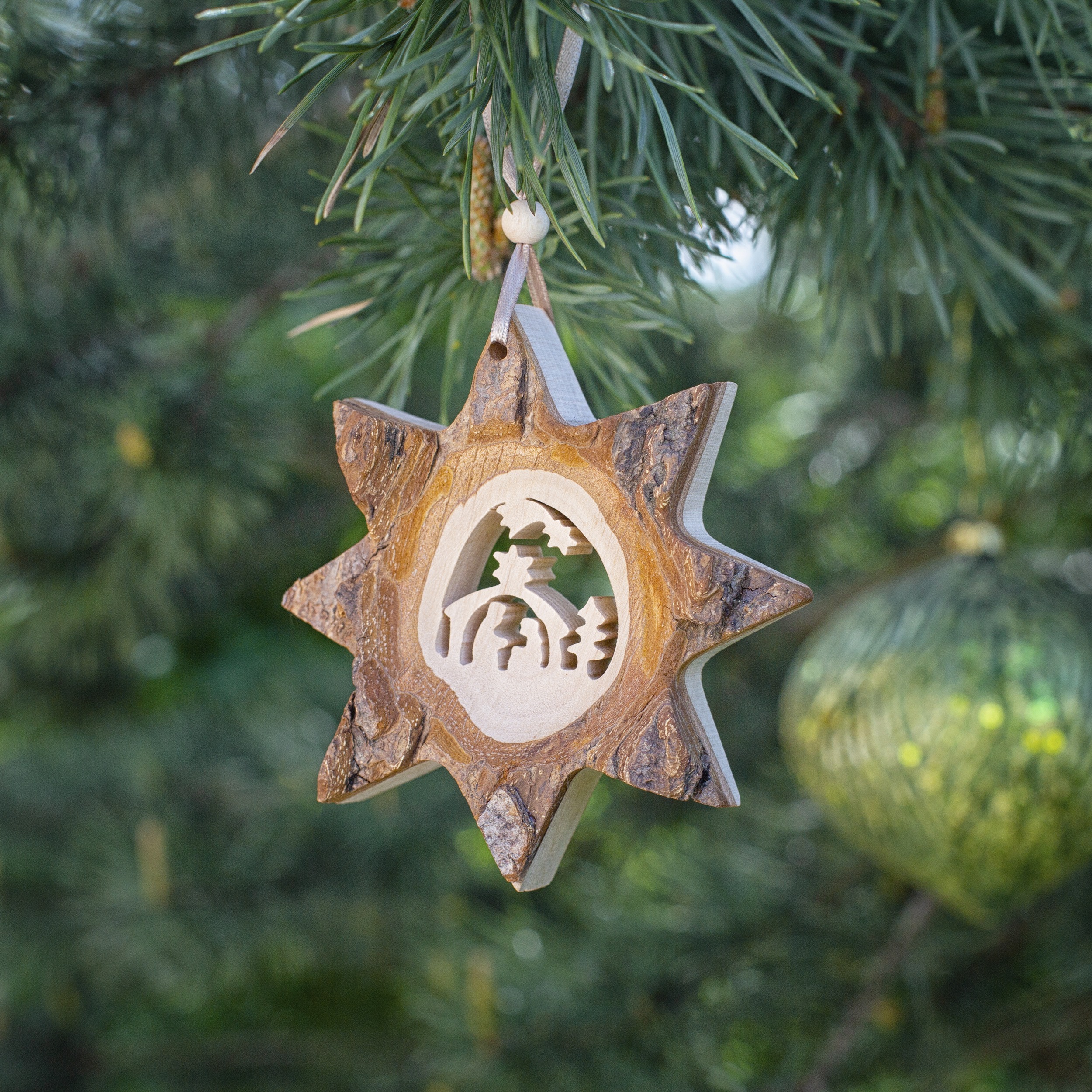 A wooden star ornament hangs on a christmas tree.