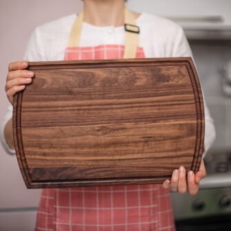A woman in an apron holding a wooden cutting board.