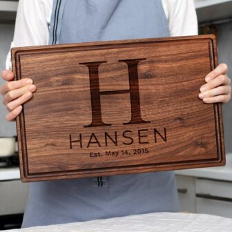 A woman holding up a wooden cutting board with the name hansen.