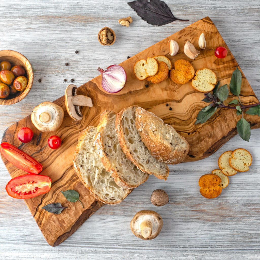 A wood cutting board with bread and vegetables on it.