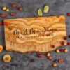 Personalized olive wood live edge cheese board laying on top of a kitchen counter surrounded by pieces of fruit.