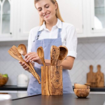 A woman in an apron holding wooden utensils.
