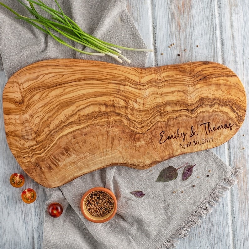 Personalized live edge olive wood cutting board with engraving in the right corner.