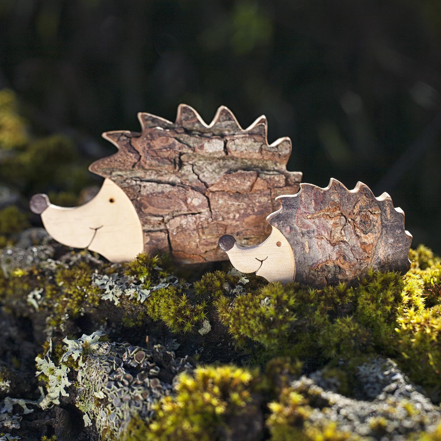 Two wooden hedgehog figurines sitting on top of moss.