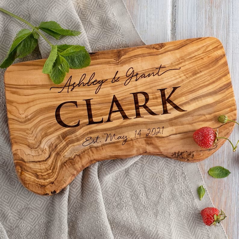 Personalized olive wood live-edge serving board featuring the engraved first and last names of the couple spanning the length of the board.