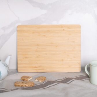 A bamboo cutting board on a kitchen countertop with teaware and cookies nearby.