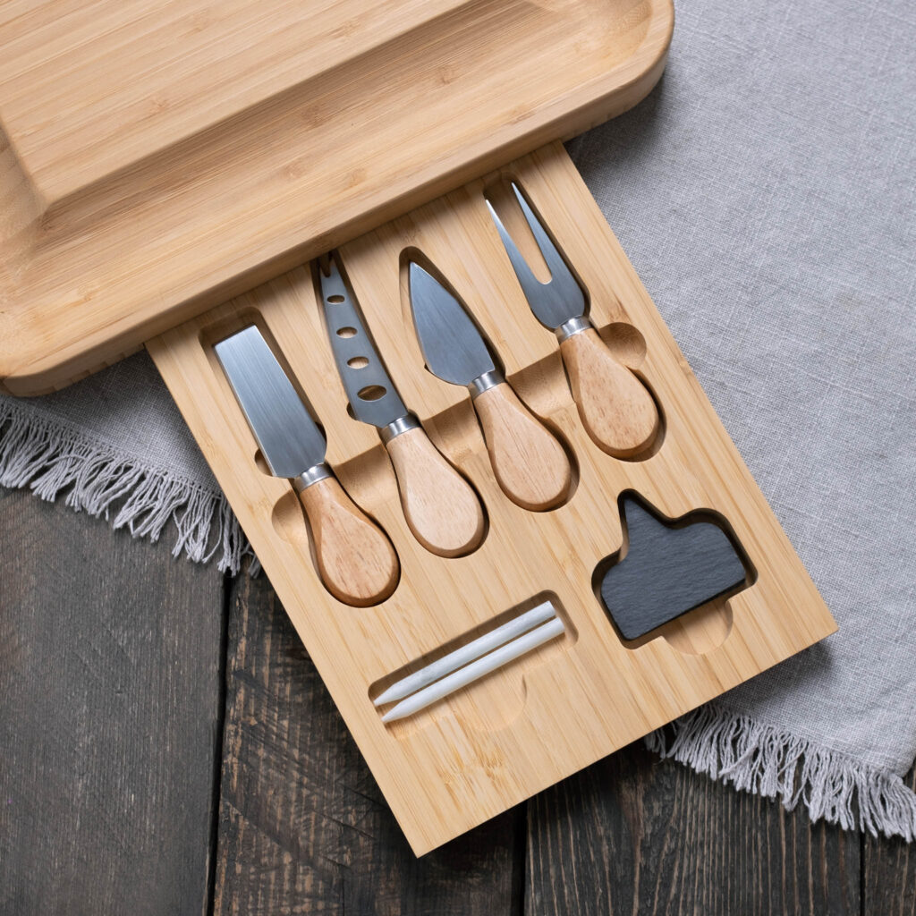 A set of cheese knives with wooden handles arranged on a bamboo cheese board.