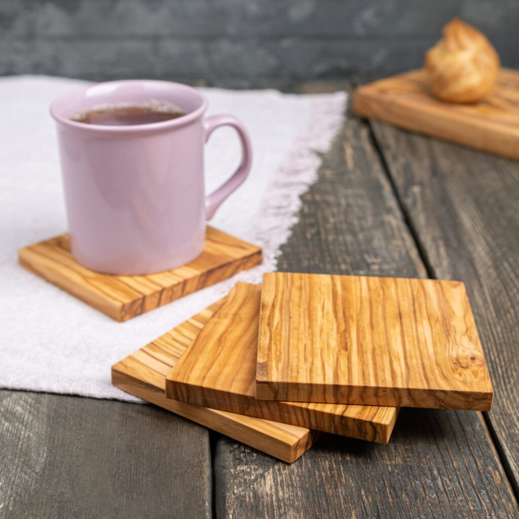 A pink mug with tea on a wooden coaster, next to another wooden coaster and a pastry on a cutting board on a rustic table.