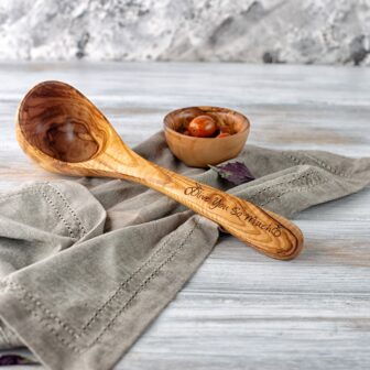 A Personalized Wooden Ladle on a table next to a bowl.